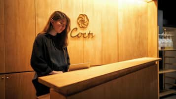 A wooden reception desk with a laptop, a woman standing behind it, and a sign with the word "Cort" on the wall.