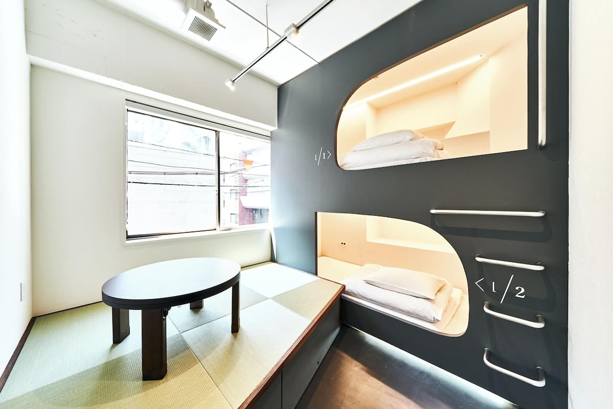 Una habitación de hotel moderna con una cama litera, una mesita pequeña y una ventana que ofrece vistas al exterior.
