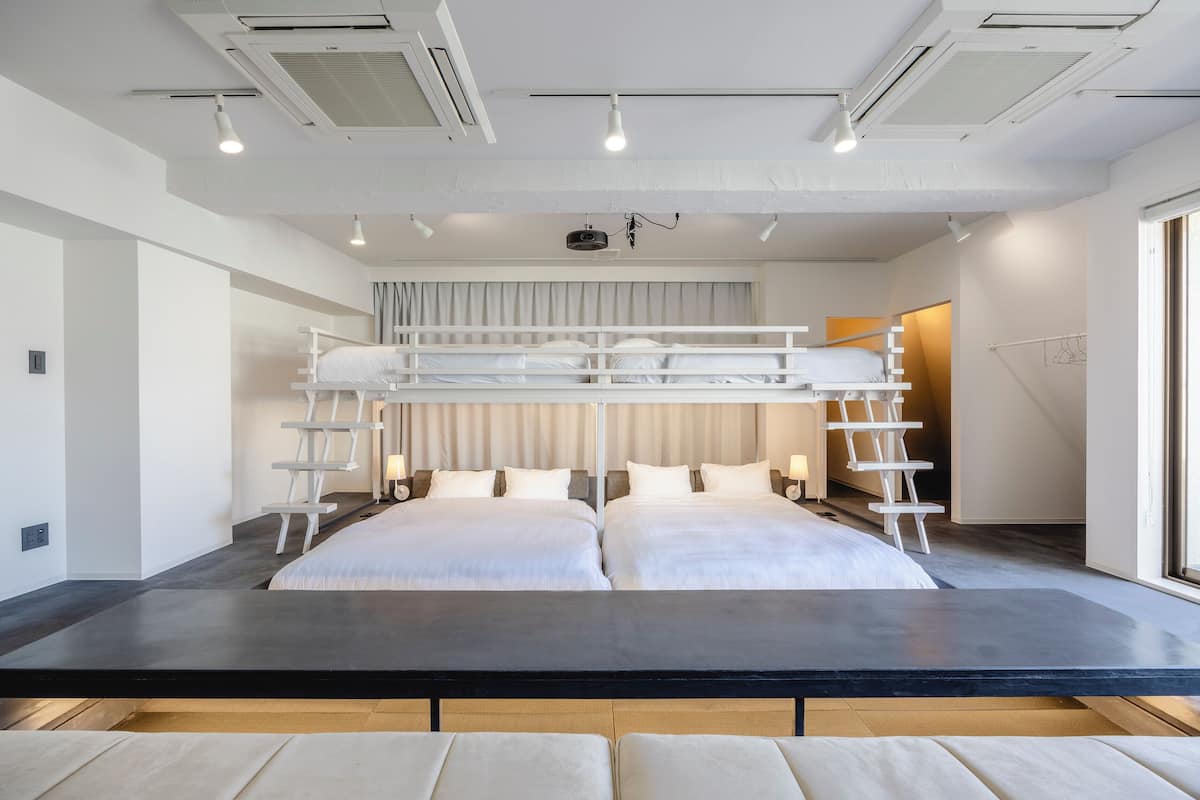 Una habitación de hotel moderna con dos camas, una mesa central negra y una cama entrepiso con escalera.