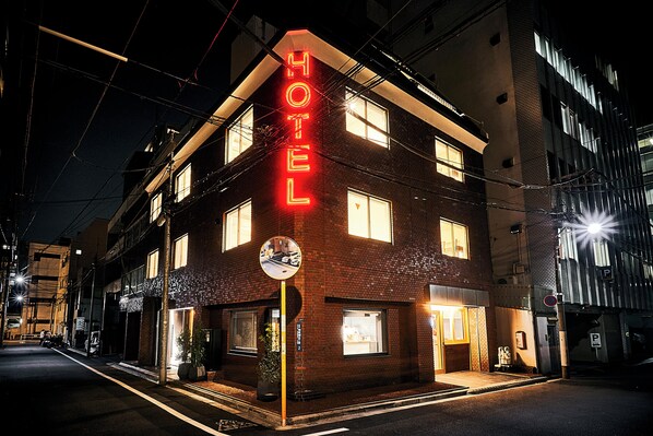 A hotel with a neon sign, multiple windows, and a street view.