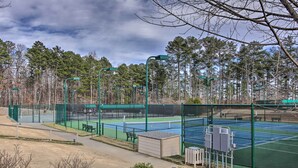 Een tennisbaan met een groene omheining, bankjes en een kleine schuur.