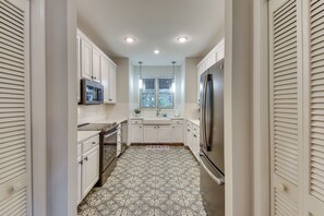 Una cocina estrecha con armarios blancos, un refrigerador de acero inoxidable y un microondas.