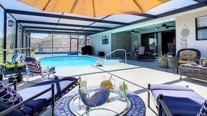 A covered outdoor pool area with lounge chairs, a table with drinks, and a decorative fish statue.