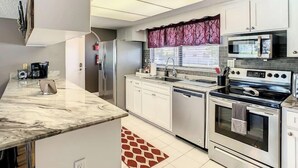 A modern kitchen with white cabinets, a stainless steel refrigerator, a microwave, an oven, and a dishwasher.