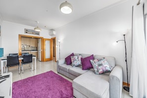 Un salon moderne avec un canapé gris, un tapis violet et un coin repas comprenant une table et des chaises.