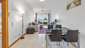 A modern living room with a sofa, dining table, chairs, and a view of the outdoors.