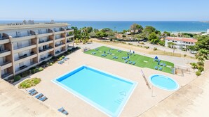 A hotel with a swimming pool, a tennis court, and a view of the sea.