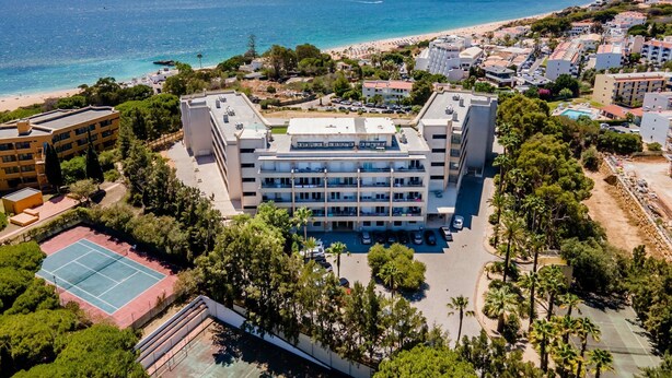 A multi-story hotel with a rooftop pool, surrounded by greenery and a beach view.