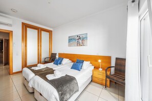 Une chambre d’hôtel avec un grand lit, une tête de lit en bois, un tableau au mur, une chaise en osier et une table de chevet avec une lampe.