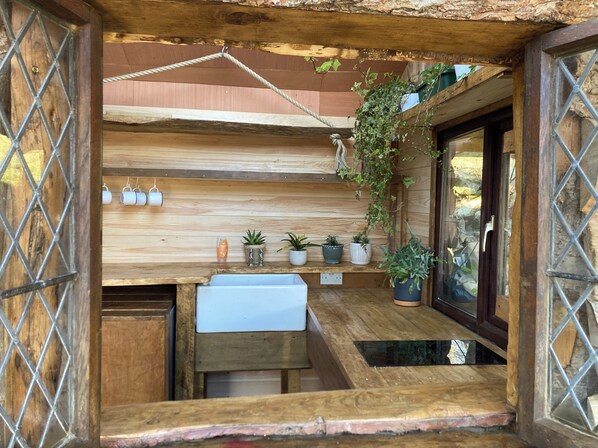 Cocina de madera rústica con pileta integrada, plantas en macetas y colgantes.