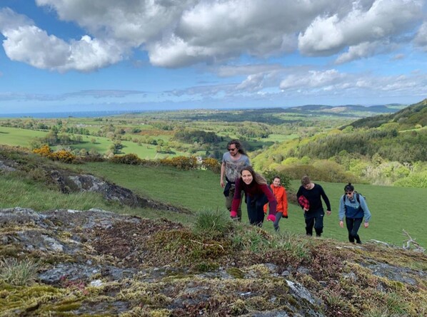 A group of people walking on a grassy hill with a scenic view of rolling hills and a partly cloudy sky. - Wood Cabin & 4 Large Bell Tents - Hapus Hideaway (Abergele)