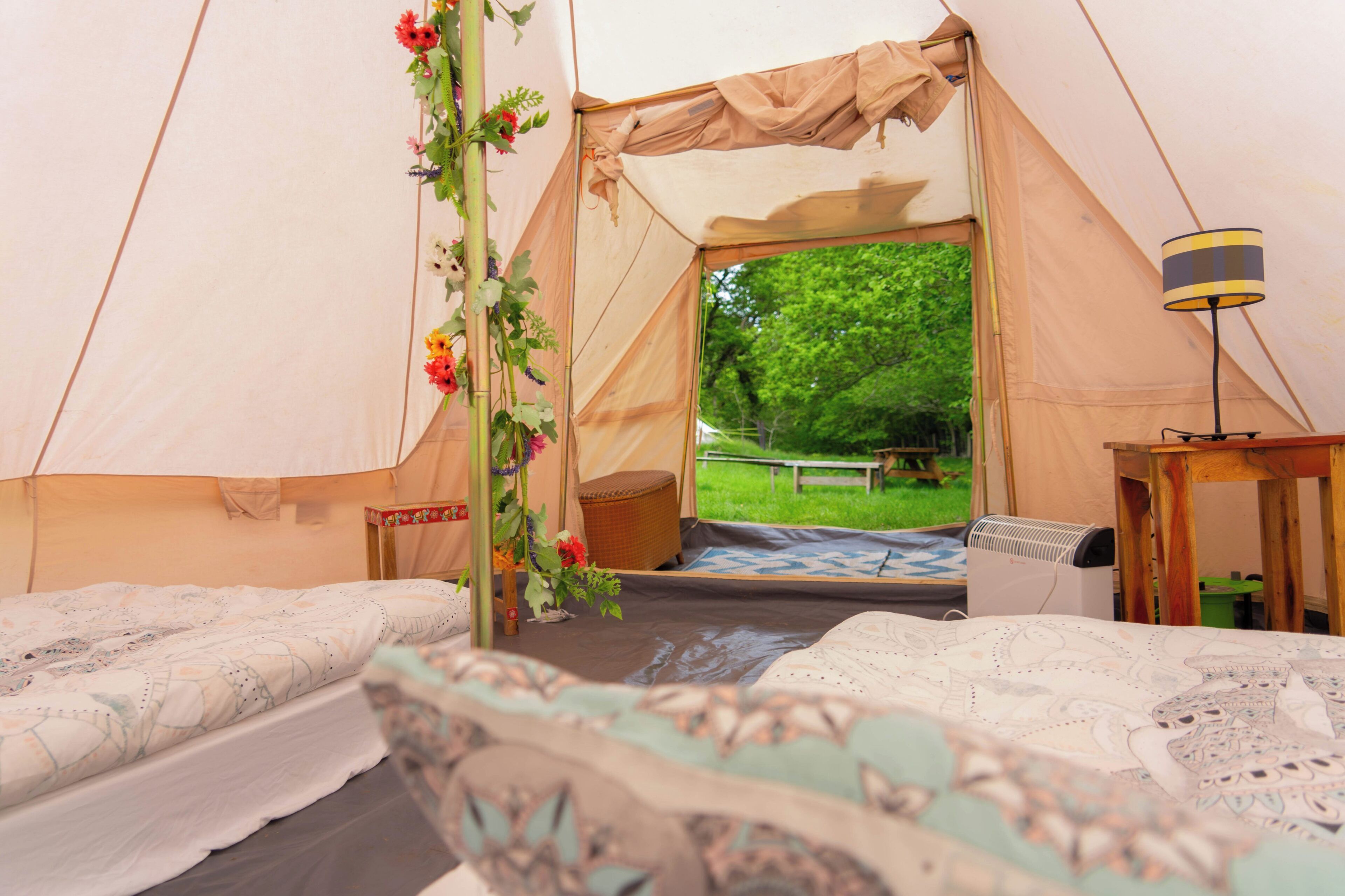 A tent with a bed, a table, and a chair. There is a window with a view of trees.