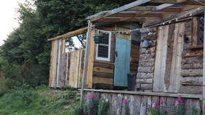 Uma cabana rústica de toras com varanda de madeira, uma janela e uma porta.