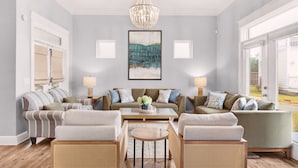 Un salon spacieux avec un haut plafond, un lustre et une grande fenêtre offrant une vue sur l’extérieur.