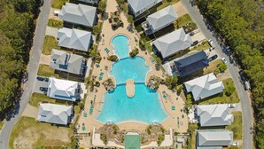 Vue aérienne d’un complexe hôtelier comprenant une piscine centrale, plusieurs bâtiments et un parking.