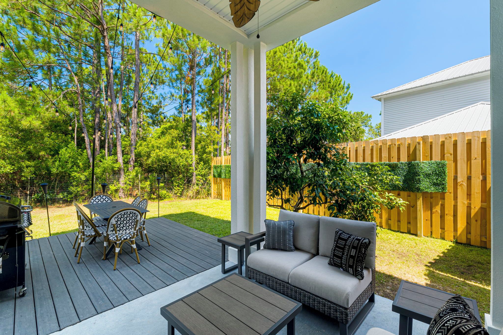 Une terrasse couverte, aménagée avec du mobilier d’extérieur, un barbecue et une clôture en bois.