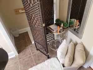 Bathroom features a woven privacy screen, a small table with mirror, and a selection of toiletries.