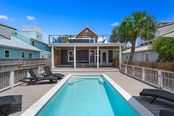A pool area with lounge chairs, a covered seating area, and a wooden deck.