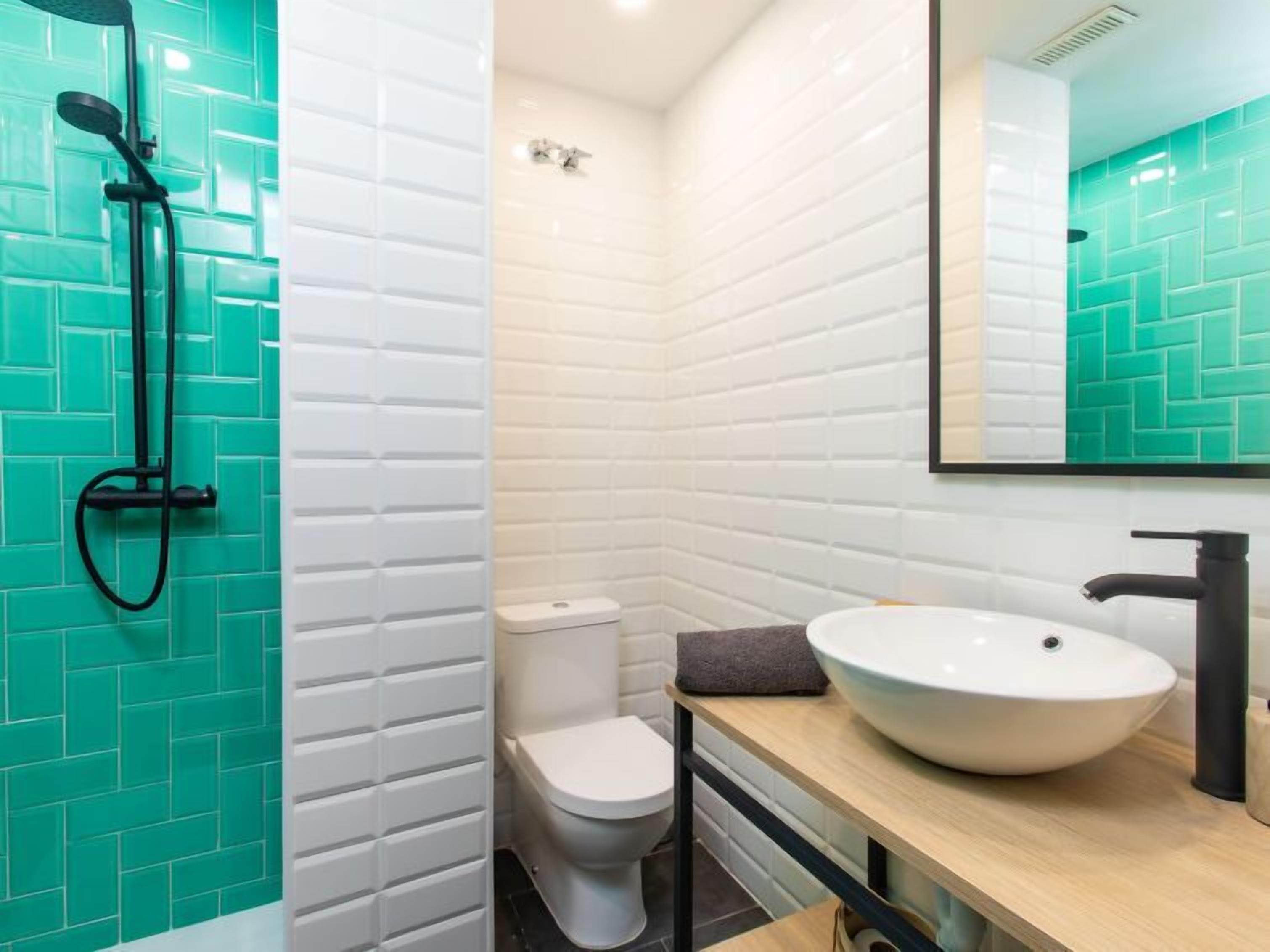 A bathroom with a white toilet, a sink with a large basin, and a shower with a black hose.