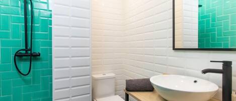 A bathroom with a white toilet, a sink with a large basin, and a shower with a black hose.