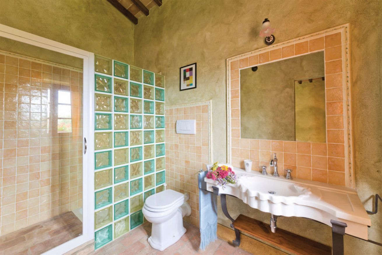 Ein Badezimmer mit weißer Toilette, einem Waschbecken mit Spiegel und einer Duschkabine mit grünen Glasfliesen.