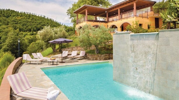 A pool with lounge chairs, a waterfall feature, and a building with a balcony.