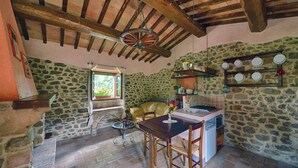 A rustic kitchen with stone walls, a wooden ceiling, a dining table with chairs, and a window.