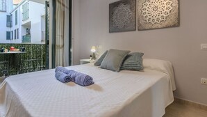 A bedroom with a bed, pillows, a nightstand, and a window with a view of buildings. - Lovely apartment for 4 guests with WIFI, A/C, TV and balcony (Tossa De Mar)
