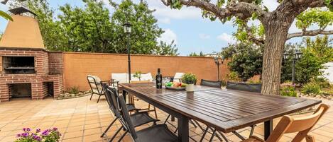 Eine Terrasse im Freien mit einem gemauerten Grill, einem Holztisch und Stühlen.