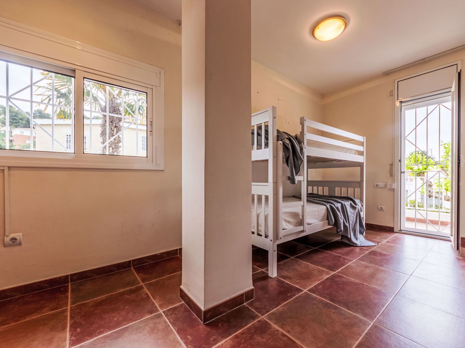 A room with a bunk bed, a window with a view of palm trees, and a door leading outside.