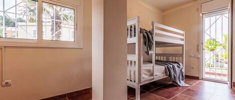 A room with a bunk bed, a window with a view of palm trees, and a door leading outside.