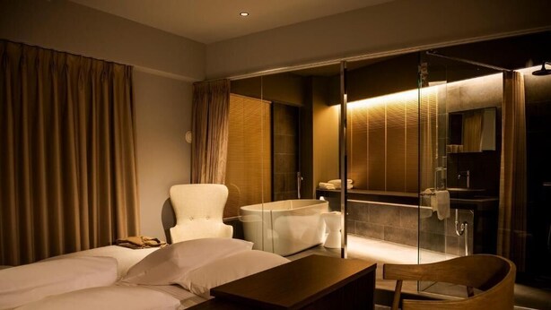 A hotel room with a bed, a wooden desk, a chair, a bathroom with a glass shower enclosure, and a large mirror. - HOTEL PETIT SUITE SOGENJI ISHIMON (Naha)