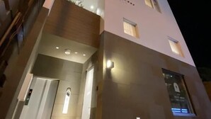 A multi-story building with a modern design, featuring a prominent entrance with a door and a small window above it. - HOTEL PETIT SUITE SOGENJI ISHIMON (Naha)