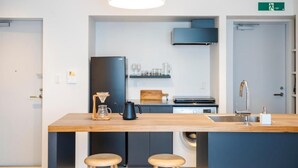 A modern kitchen with a wooden island, bar stools, a built-in washing machine, and a dark-colored refrigerator. - HOTEL PETIT SUITE SOGENJI ISHIMON (Naha)