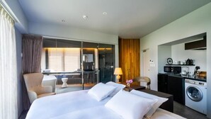 A hotel room with a large bed, a desk, a chair, a washing machine, and a kitchenette. - HOTEL PETIT SUITE SOGENJI ISHIMON (Naha)