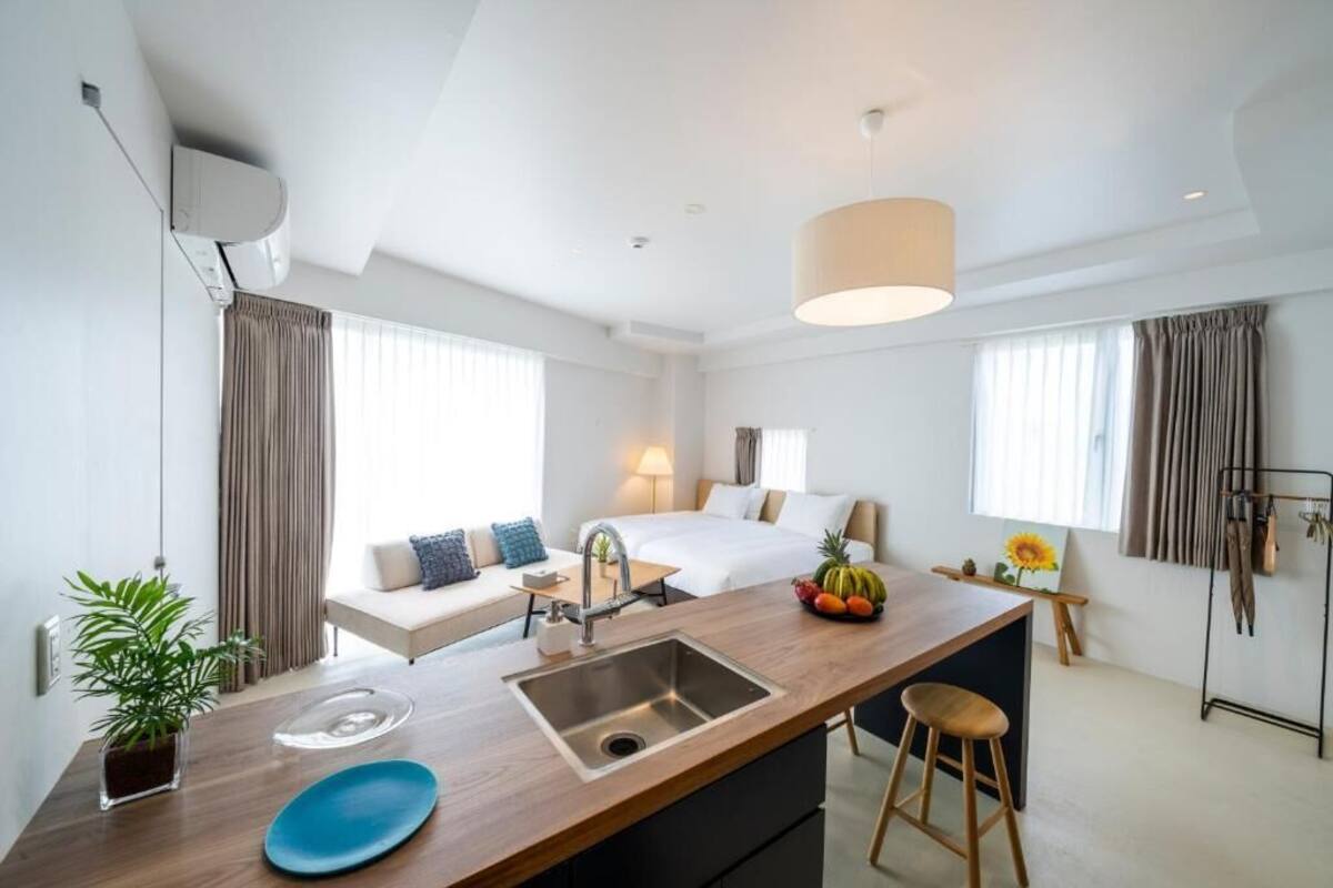 A modern hotel room with a kitchenette, a bed, a sofa, and a dining area.