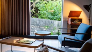 A modern room with a large window, a round table, a blue armchair, and a lamp on a side table. - HOTEL PETIT SUITE SOGENJI ISHIMON (Naha)