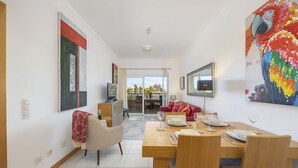 Un salon moderne comprenant un coin repas, un téléviseur et une grande œuvre d’art colorée accrochée au mur.