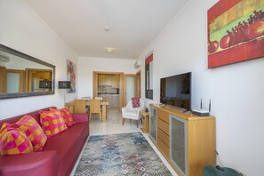Un salon moderne avec un canapé rouge, un téléviseur et une cuisine en arrière-plan.