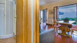 A room with a wooden floor, a grey sofa, a dining table with chairs, and a view of the sky through a large window. - Beautiful apartment for 4 guests with WIFI, pool, terrace, pets allowed and panoramic view (Lamporecchio)