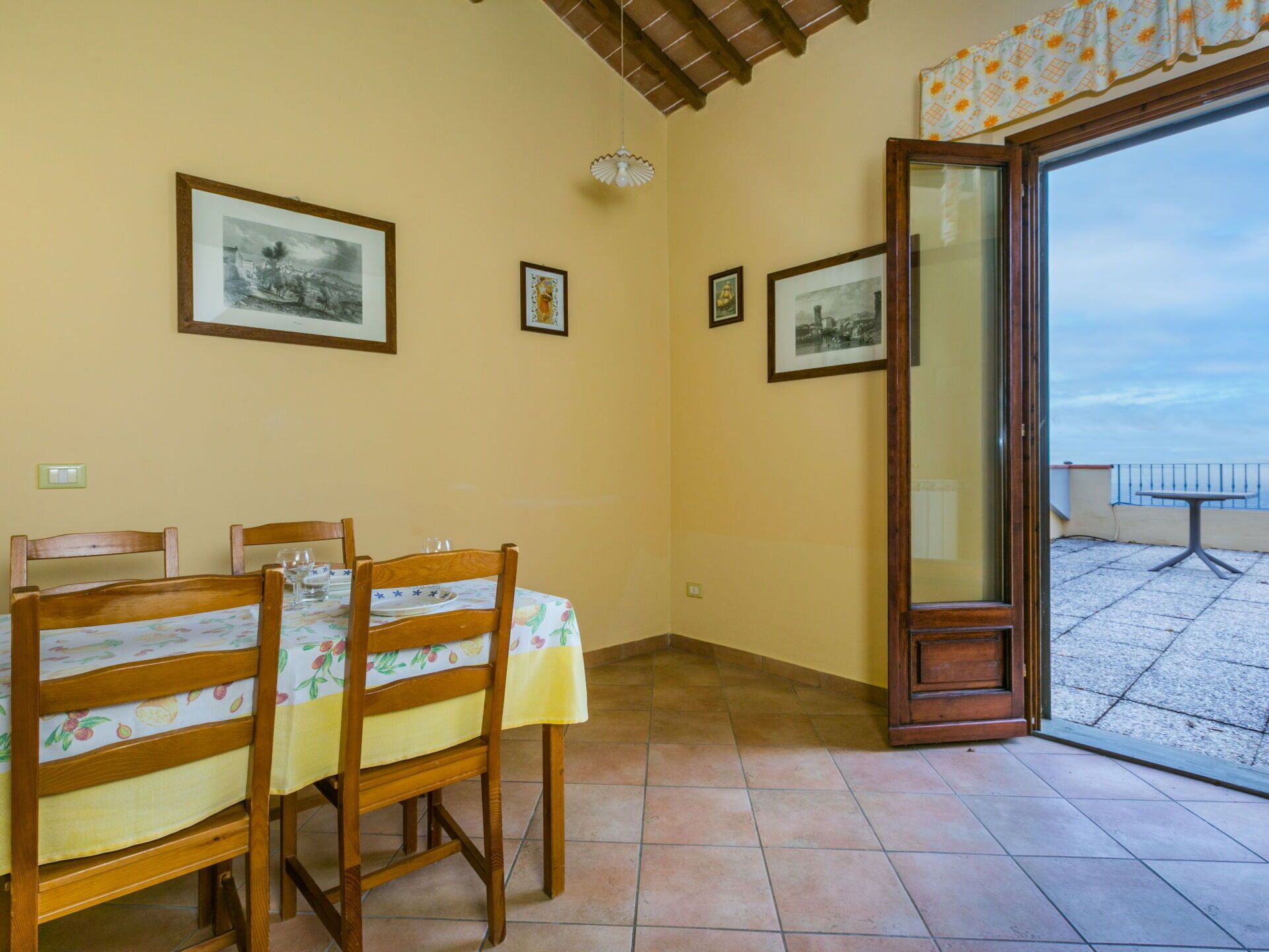 A dining area with a table set for two, wooden chairs, and a balcony with a view.