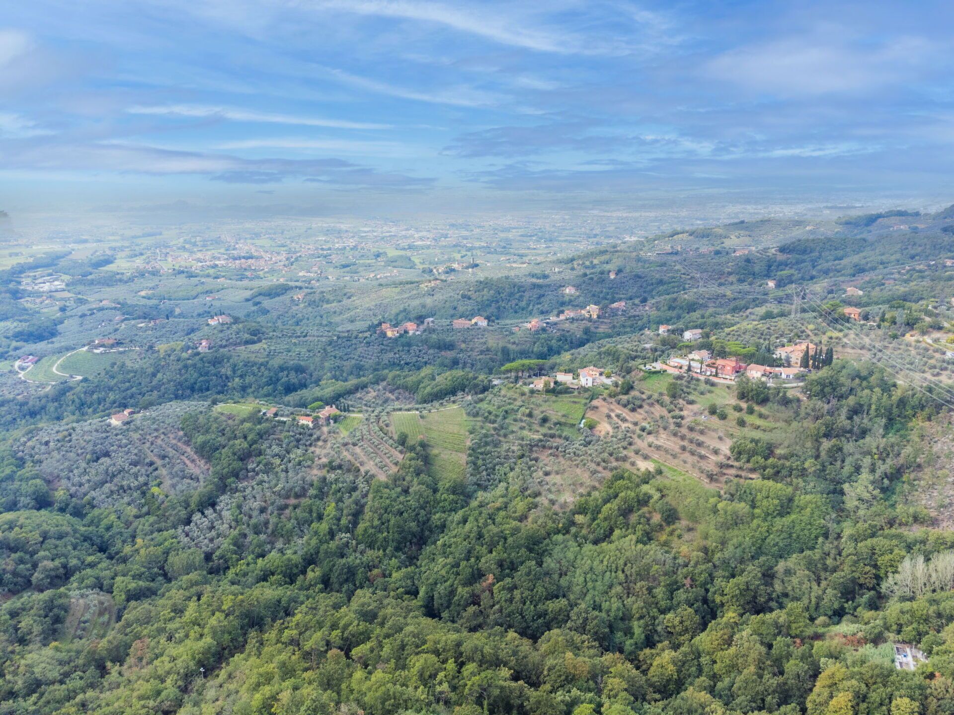 A panoramic view of a hilly landscape with scattered buildings, roads, and patches of greenery.