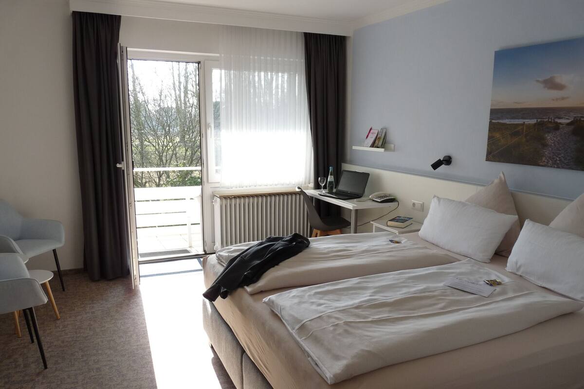 Hotellihuone, jossa on kaksi sänkyä, työpöytä kannettavalla tietokoneella, tuoli ja näkymä ulos.