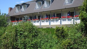 Een hotel met een plat dak, meerdere balkons met rode bloemen en een witte gevel.