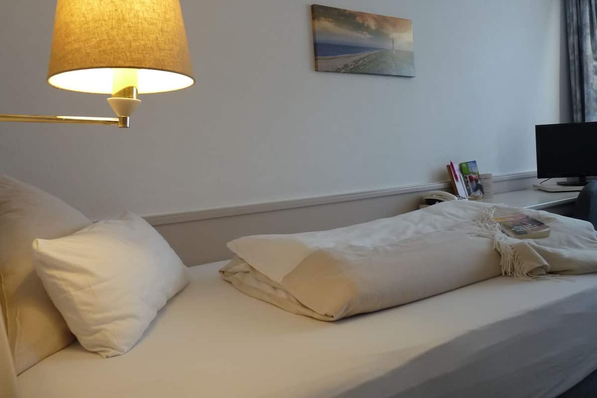 Hotellihuone, jossa on sänky, lamppu, taulu, työpöytä tietokoneella ja ikkuna, jossa on verhot.
