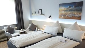 Hotelkamer met twee bedden, een bureau, een stoel, een nachtkastje en een wandplank met spullen.