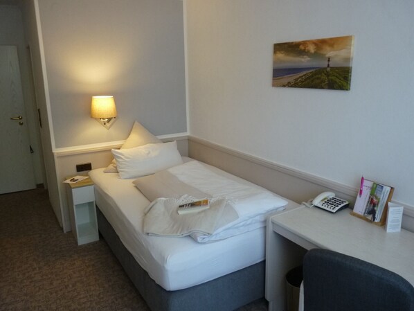 Habitación de hotel con cama, mesita de noche, lámpara y un cuadro en la pared.