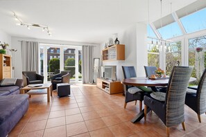 Una sala de estar moderna con un sofá, sillas, una mesa de comedor, un televisor y una estantería.