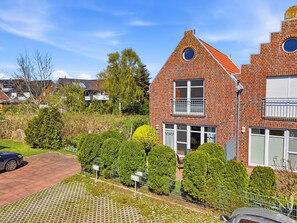 A two-story brick house with a red-tiled roof, a balcony, and a small circular window.