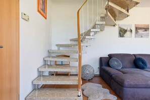 Un escalier avec des rampes en métal et une main courante en bois, menant à un espace de vie comprenant un canapé et des coussins.